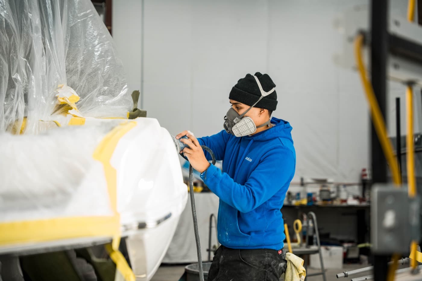 Technician in a respirator sanding a masked boat hull for gel coat repair